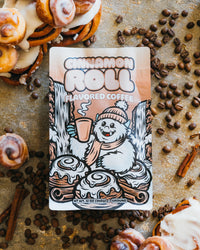 Cinnamon roll flavored coffee package surrounded by cinnamon rolls and coffee beans on a rustic background