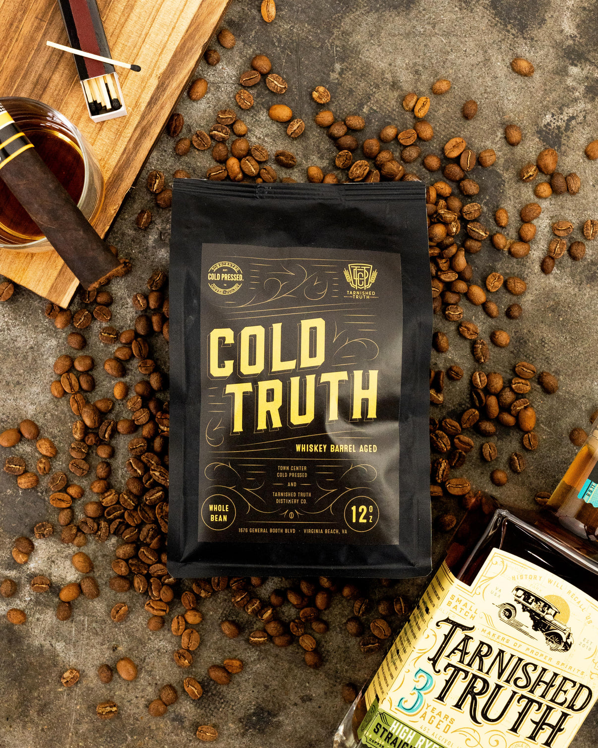 Cold Truth coffee package surrounded by coffee beans & whiskey products on a rustic surface.