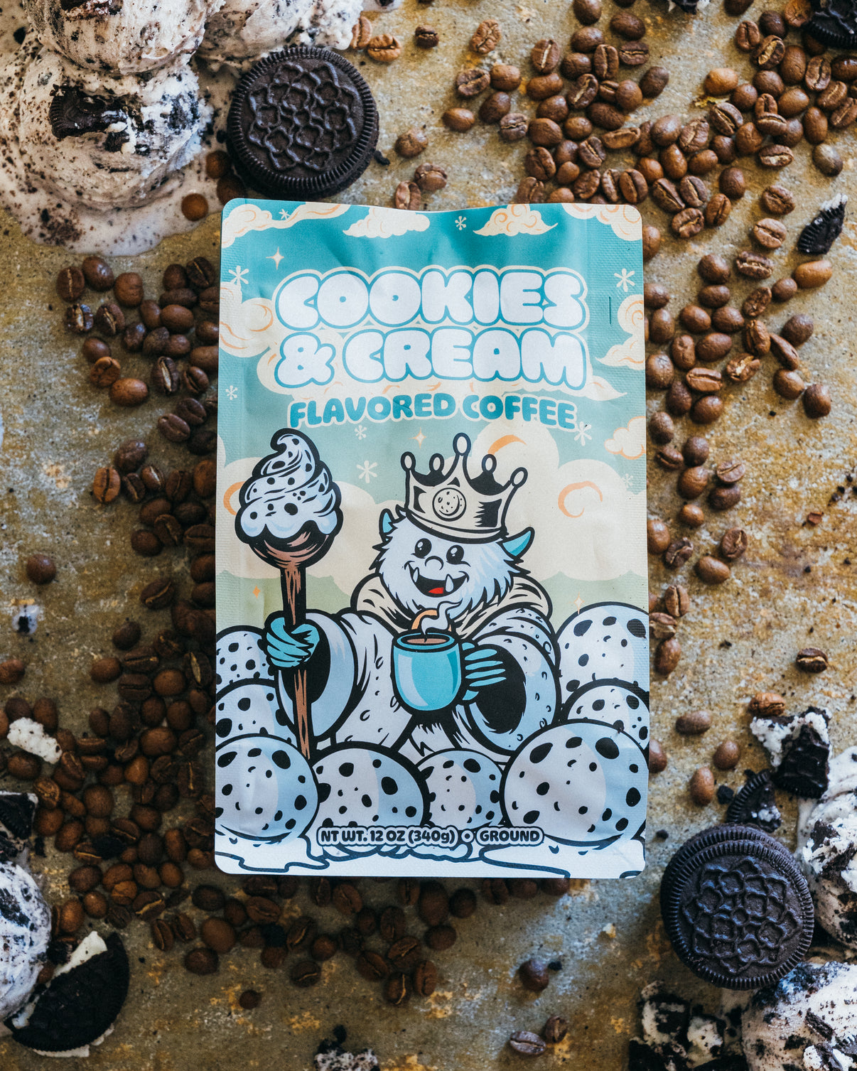 Cookies & Cream flavored coffee package surrounded by cookies, cream, and coffee beans on a rustic surface.