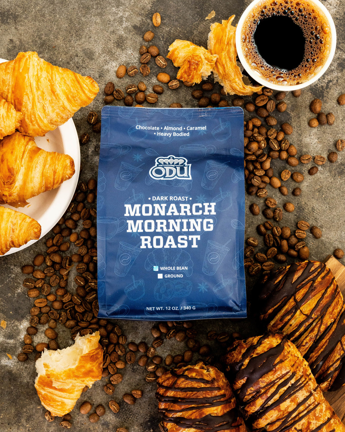 ODU Monarch Morning Roast coffee package with croissants and coffee beans on a rustic surface