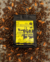 Coffee bag labeled 'Pure Black Bold Roast' surrounded by coffee beans on a textured surface.